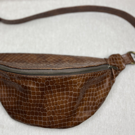 A brown faux-crocodile leather fanny pack with a dark metal zipper and strap, shown on a light gray textured background.