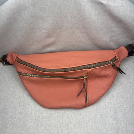 A peach-colored leather fanny pack with multiple zippered compartments and a dark strap, laid flat on a light gray textured fabric background.