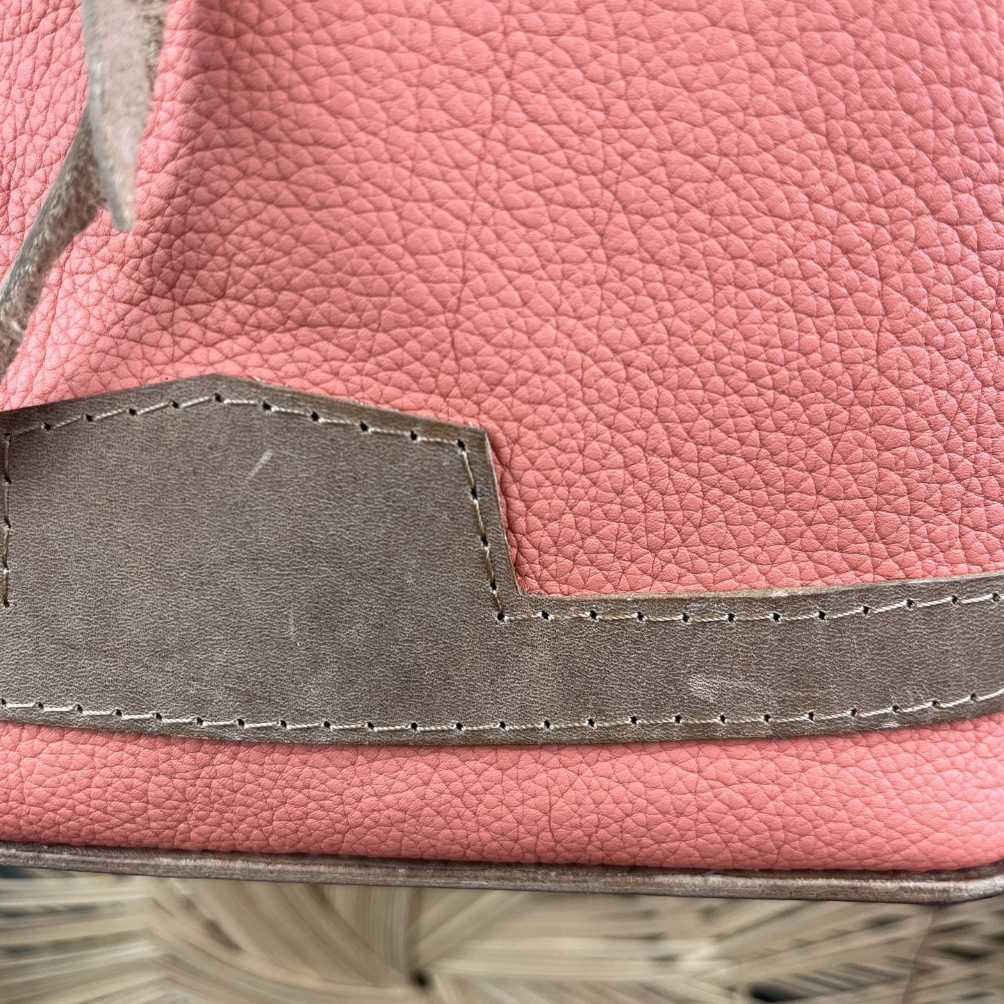 Close-up of a pink pebbled leather bag with a contrasting taupe-brown stitched leather accent piece.