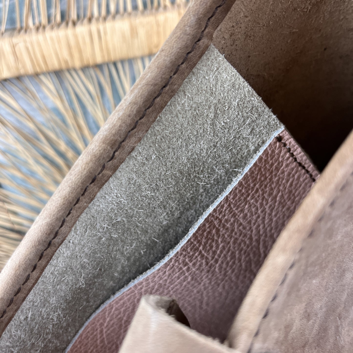 Close-up detail of a leather bag showing the interior lining with a textured gray suede-like layer and a brown pebbled leather section, with stitching along the edge.