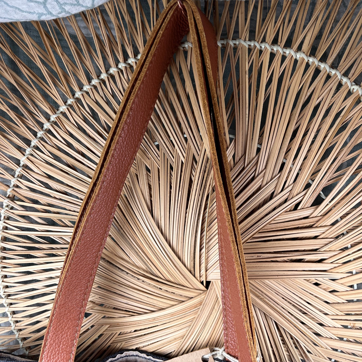Close-up of a woven straw or palm-leaf style bag with a brown leather strap arching through the center.
