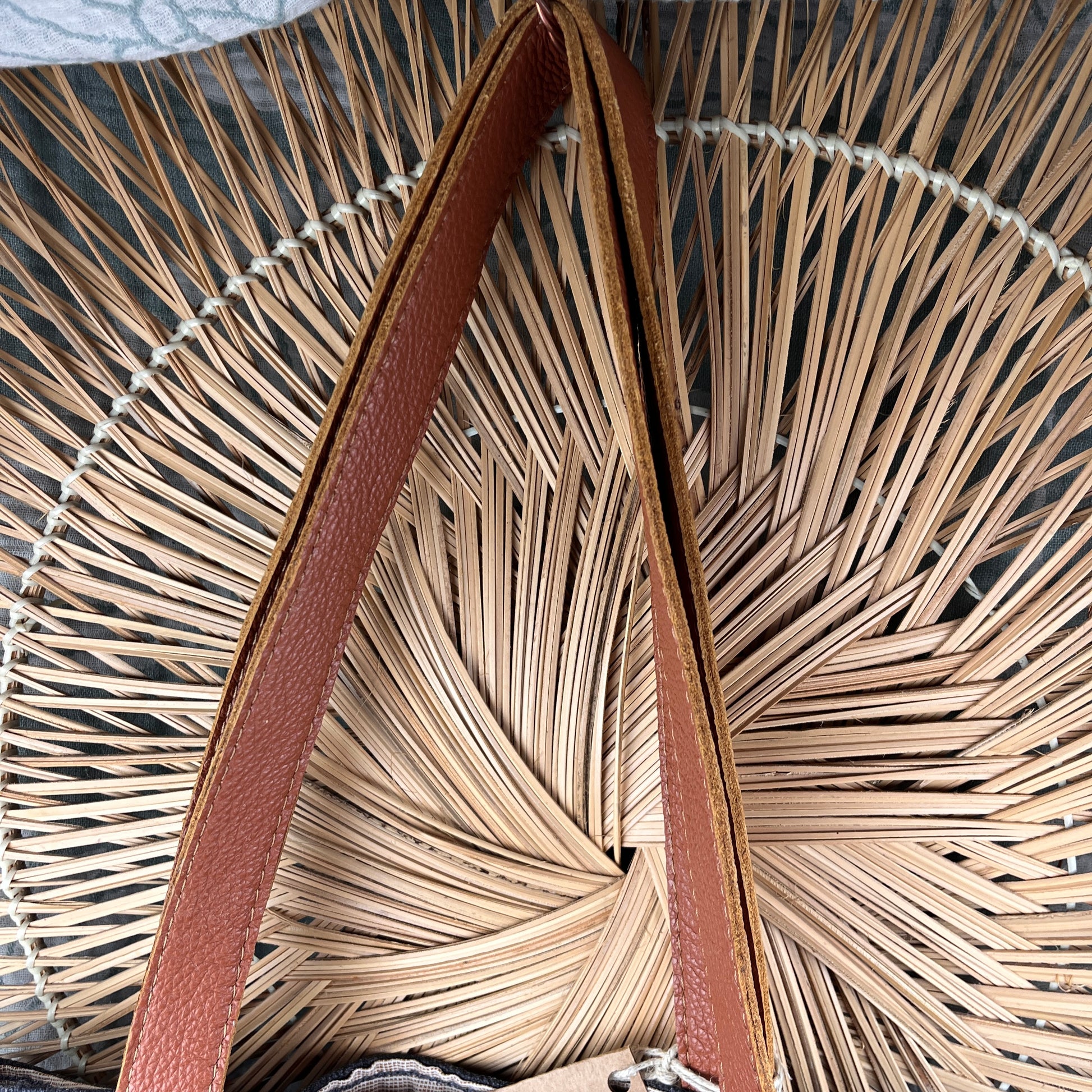 Close-up of a woven straw or palm-leaf style bag with a brown leather strap arching through the center.