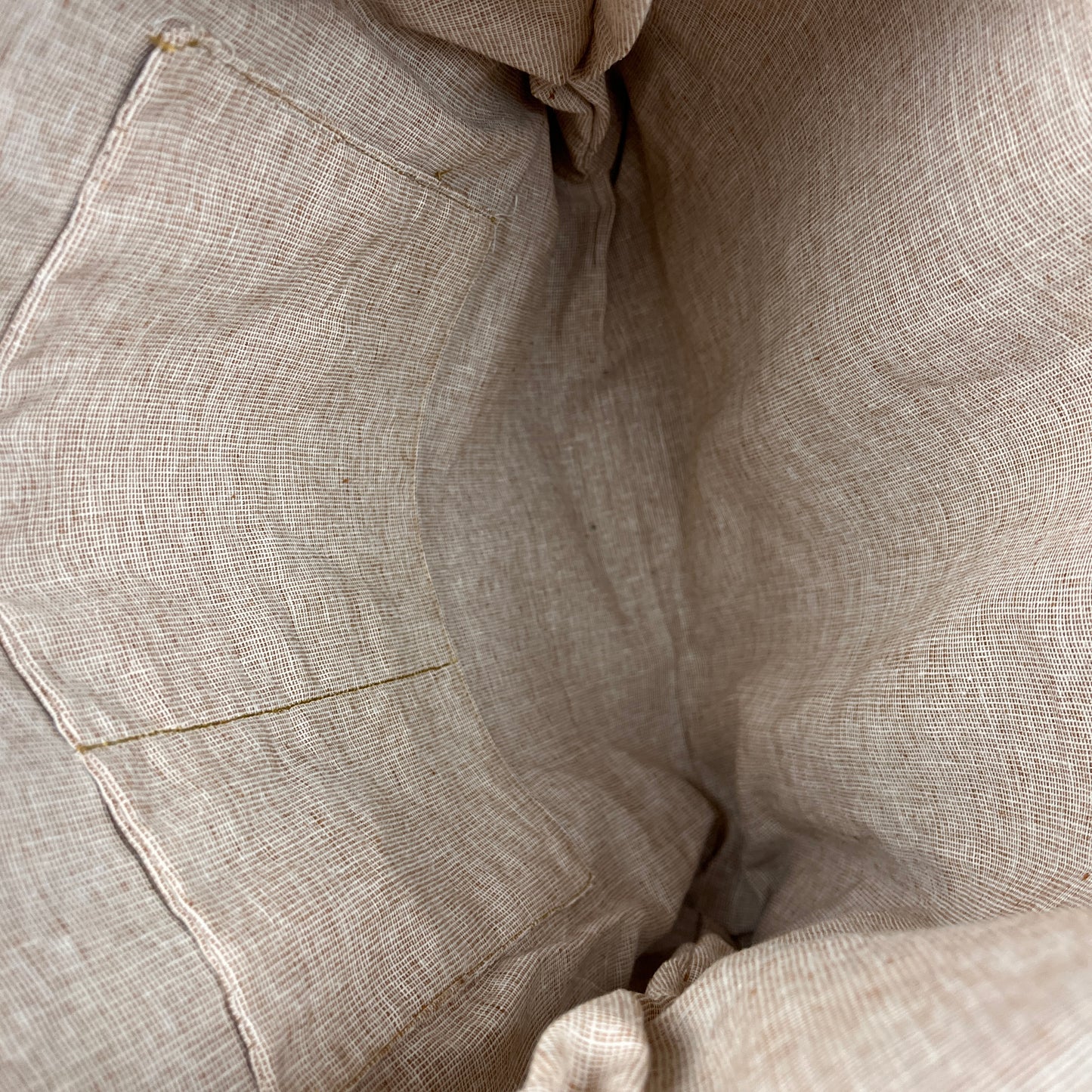 Close-up of a light beige linen fabric with a visible stitched pocket and textured weave.