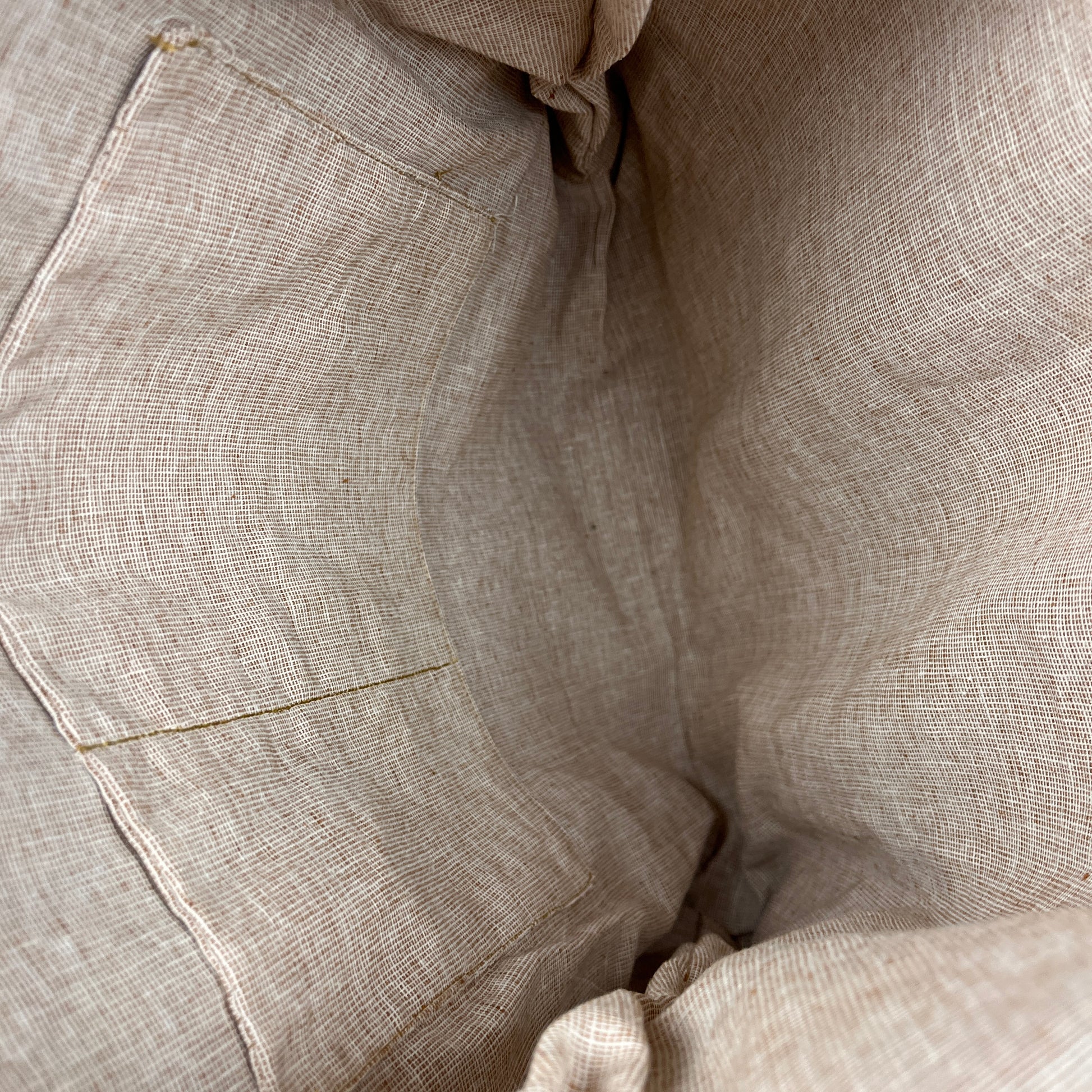 Close-up of a light beige linen fabric with a visible stitched pocket and textured weave.