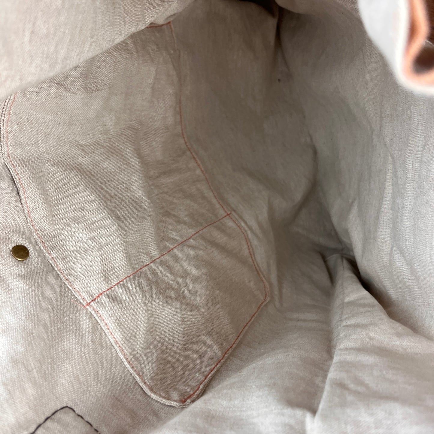Close-up of a light beige linen garment with a pocket, showing the fabric texture and contrast stitching.