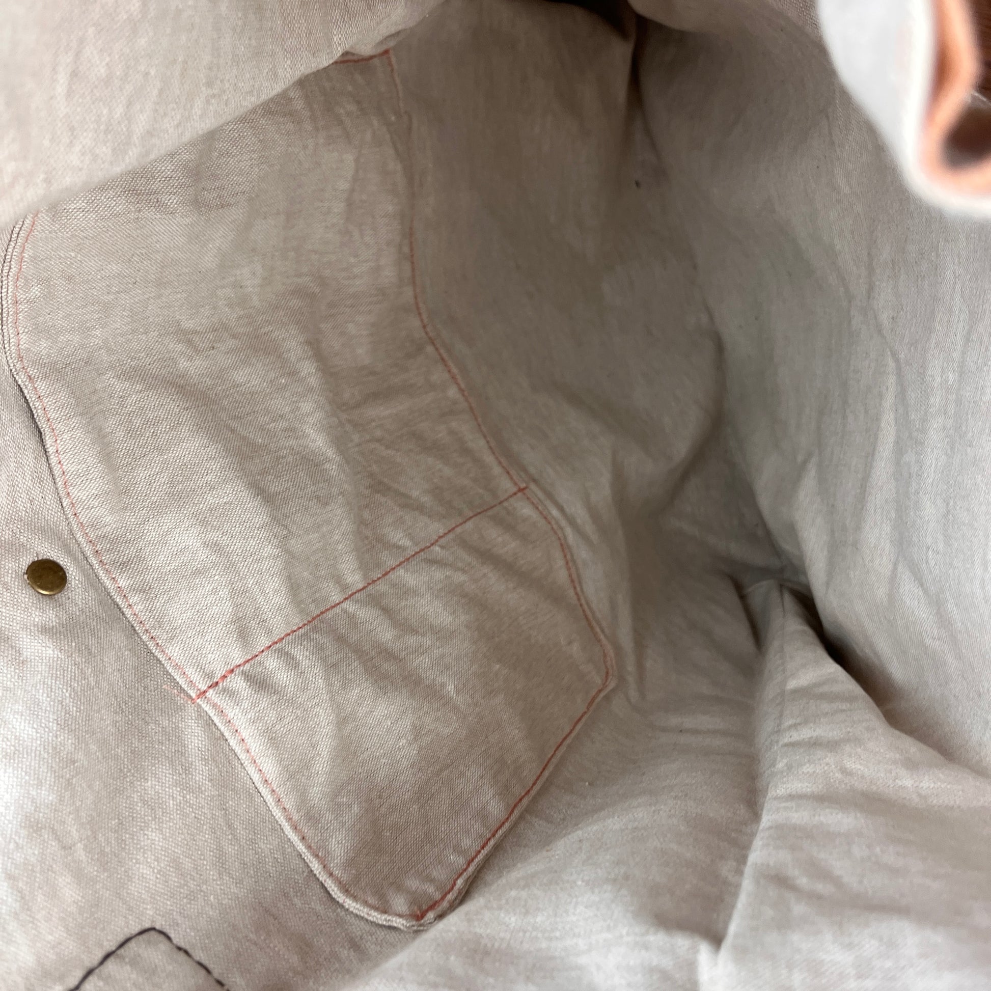 Close-up of a light beige linen garment with a pocket, showing the fabric texture and contrast stitching.