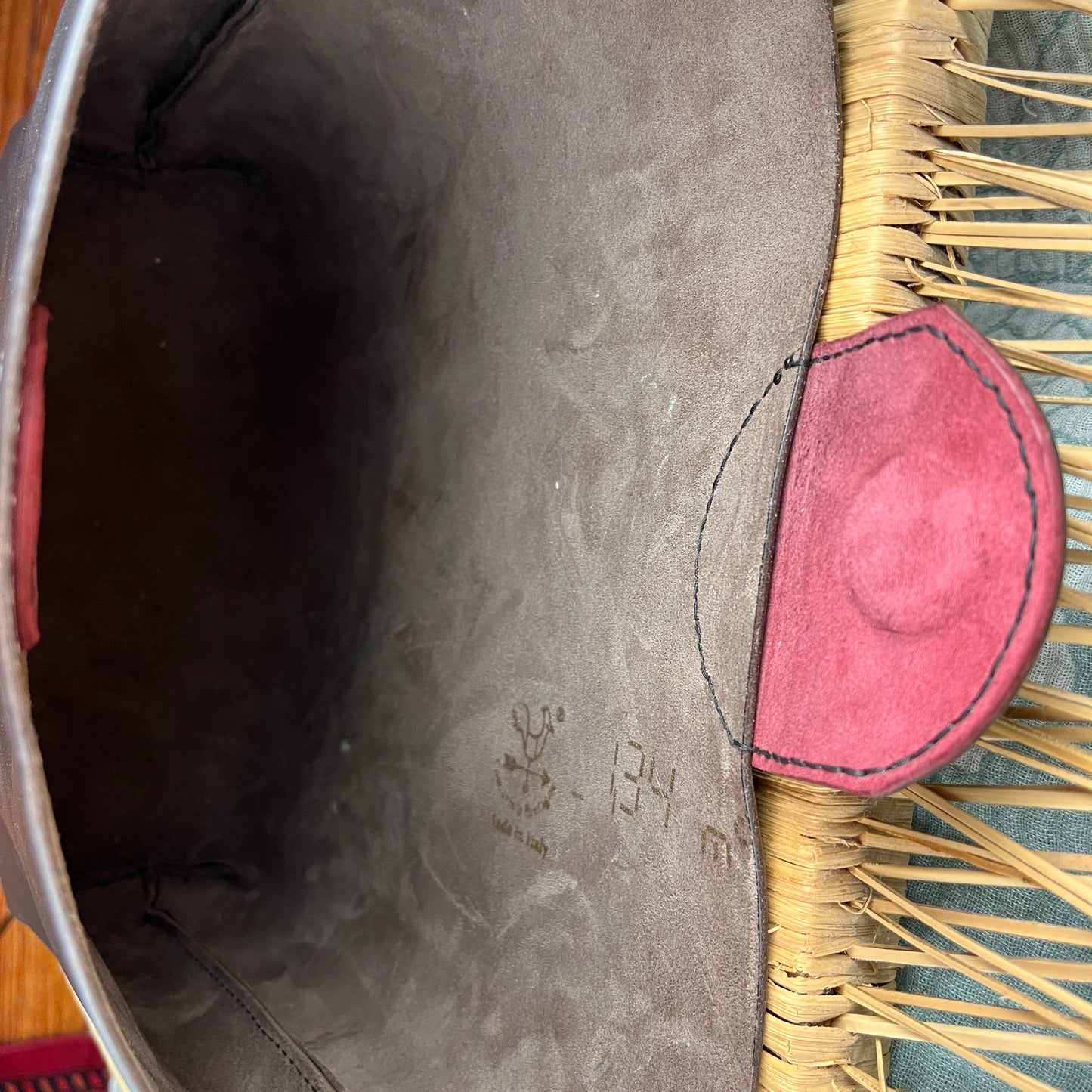 Close-up of the interior of a woven basket or hat, showing a dark brown suede-like lining, a red fabric trim, and natural tan wicker strands.