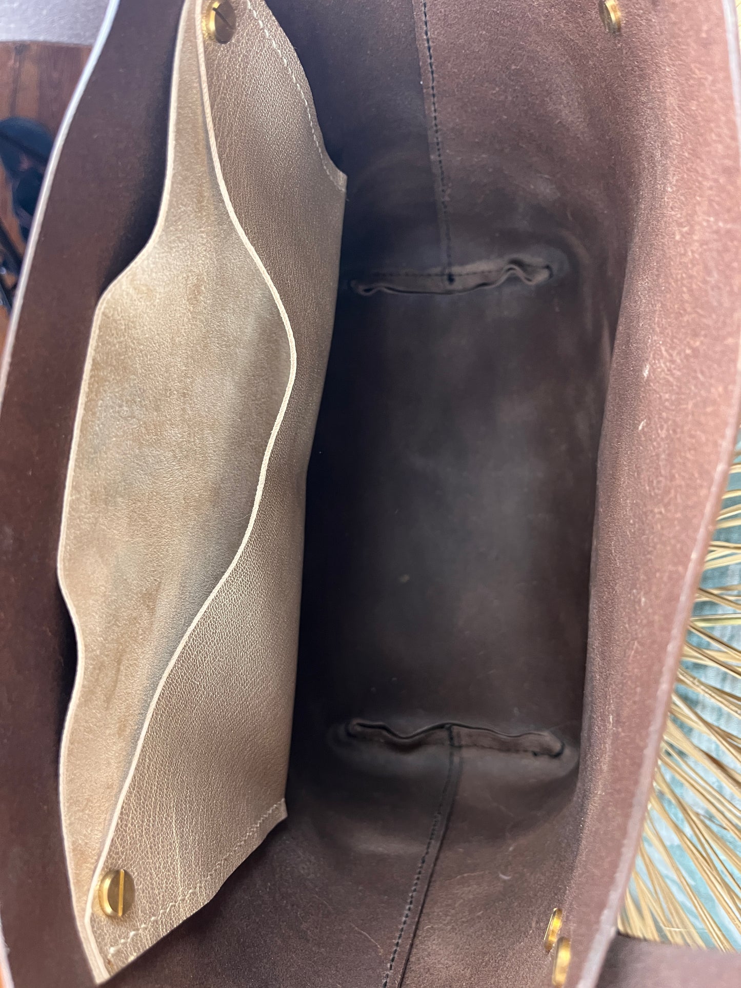 Close-up view inside a brown leather bag, showing a beige suede or nubuck interior organizer panel with gold-tone snap hardware.